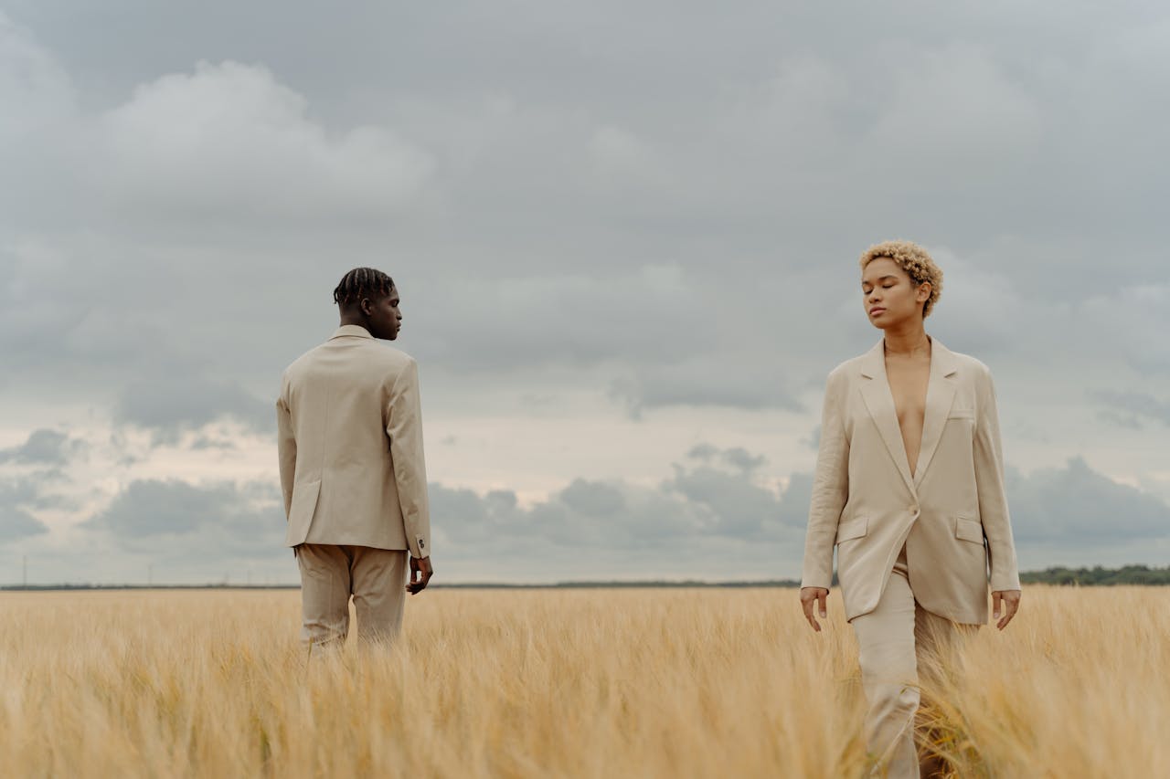 Stylish individuals in suits posing in a serene meadow under a cloudy sky.